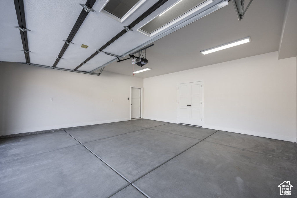 Spacious garage with concrete flooring, multiple overhead lights, a double-panel interior door, and a single-panel interior door