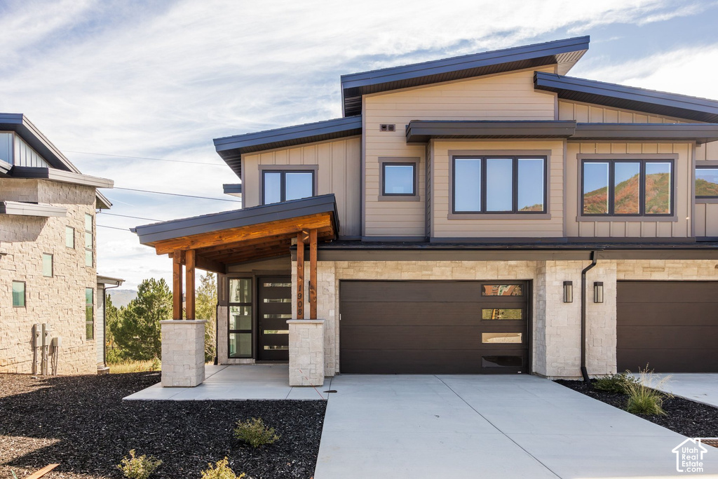 Modern exterior with a sloped roofline, wood-clad entryway, stone accents, and dark-framed windows