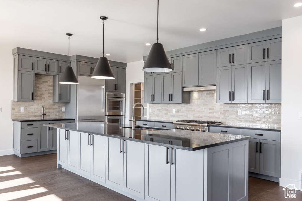 Spacious kitchen featuring an expansive center island, gray cabinetry with dark hardware, stainless steel appliances, and a tiled backsplash