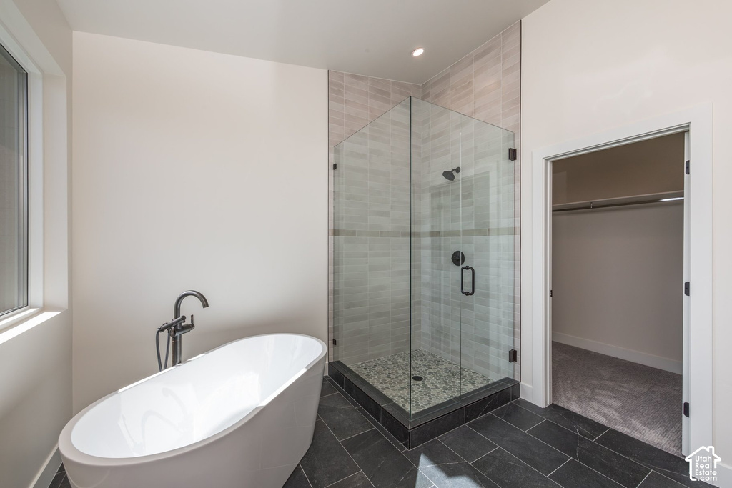 Freestanding soaking tub with floor-mounted faucet, glass-enclosed shower with tiled walls and pebble flooring, and large format dark tile flooring
