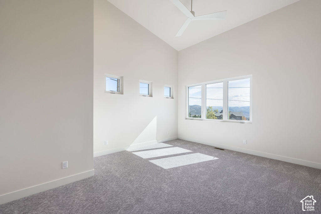 Vaulted ceiling with a ceiling fan, three transom windows, a large multi-pane window, and gray patterned carpeting