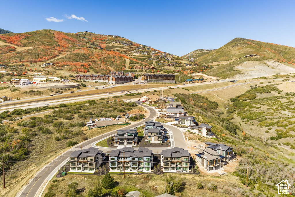 Multiple residential structures situated on a winding paved road, surrounded by hills with varied natural vegetation and distant structures