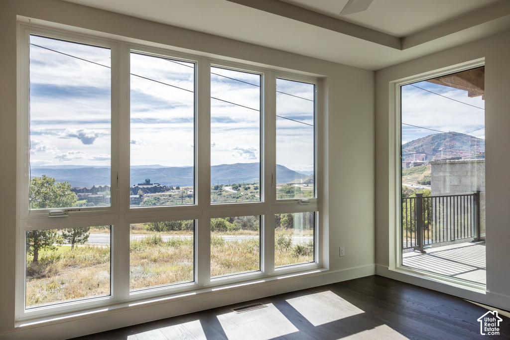 Expansive windows, tray ceiling, dark wood-finish flooring, and private balcony with metal railings