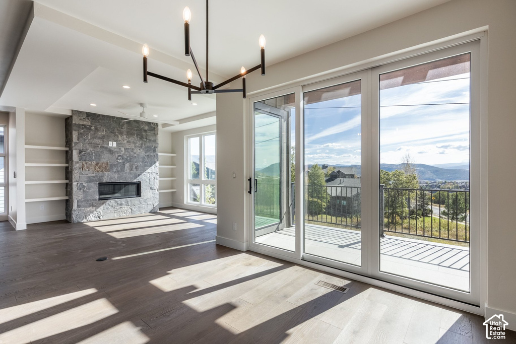 Spacious room featuring wood-finish flooring, a stone-clad fireplace, integrated shelving, a contemporary chandelier, and expansive sliding glass doors leading to a balcony