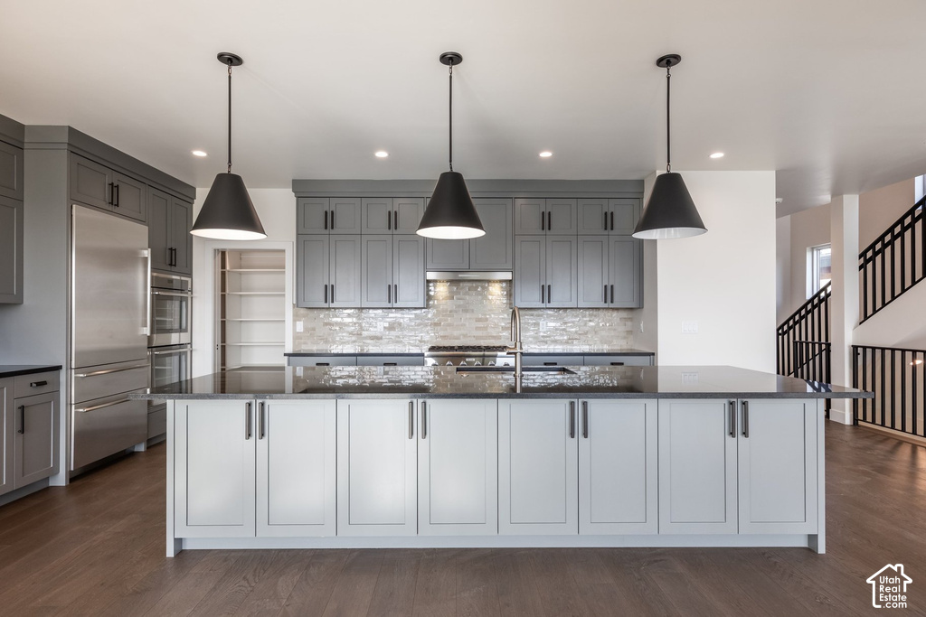 Spacious kitchen featuring an expansive center island, pendant lighting, stainless steel appliances, and wood-finish flooring