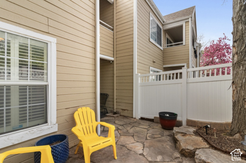 Exterior patio featuring flagstone paving, a white privacy fence, and a second-story balcony