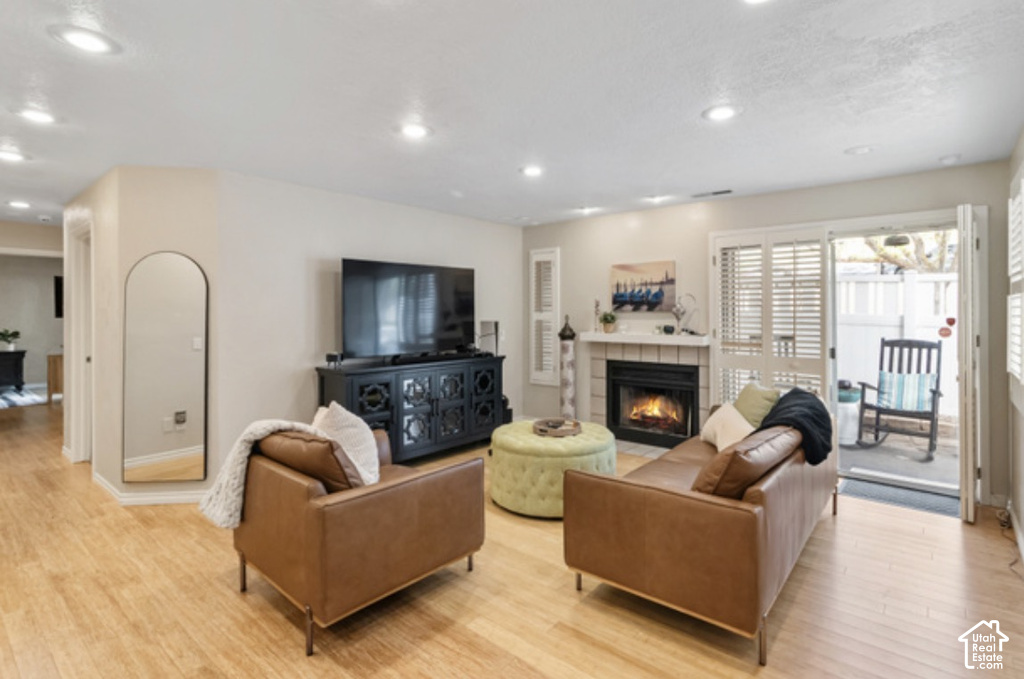 Wood-finish flooring throughout, recessed ceiling lighting, fireplace with a tiled surround, and sliding glass doors with interior shutters