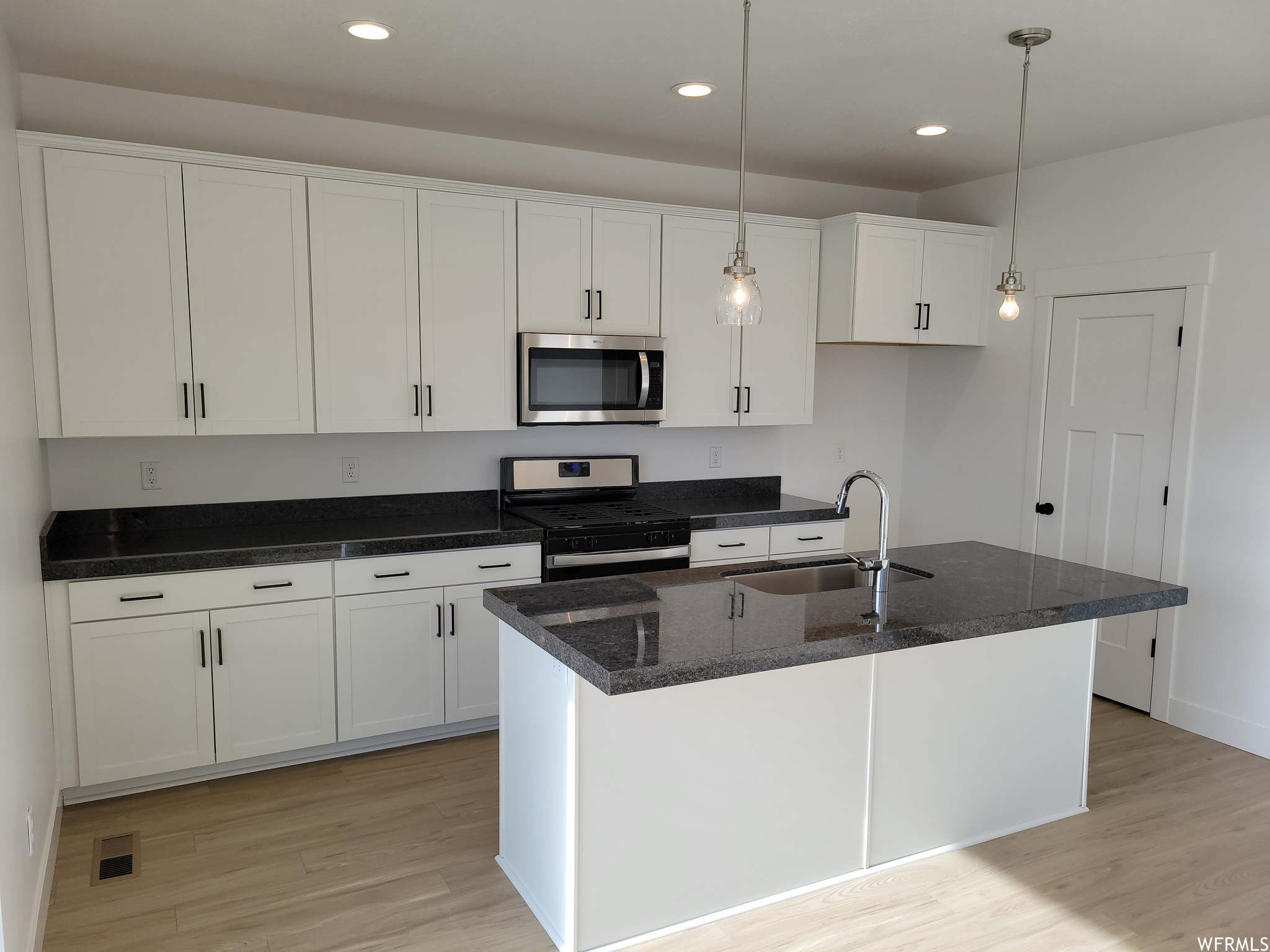 Kitchen with wood-type flooring, microwave, range oven, white cabinets, pendant lighting, and dark stone countertops