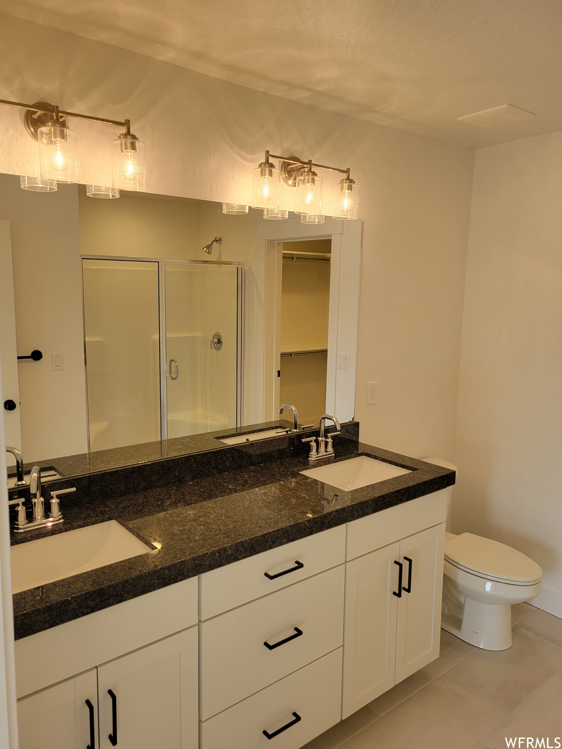 Bathroom featuring tile floors, toilet, double sink vanity, a shower, and dual mirrors