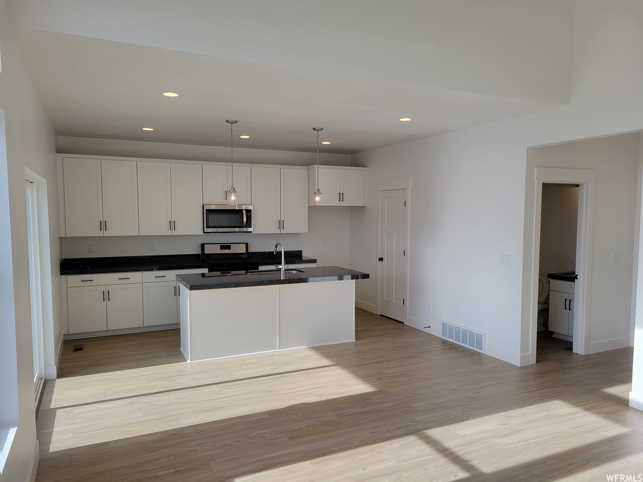 Kitchen featuring hardwood floors, microwave, range oven, dark countertops, pendant lighting, and white cabinetry