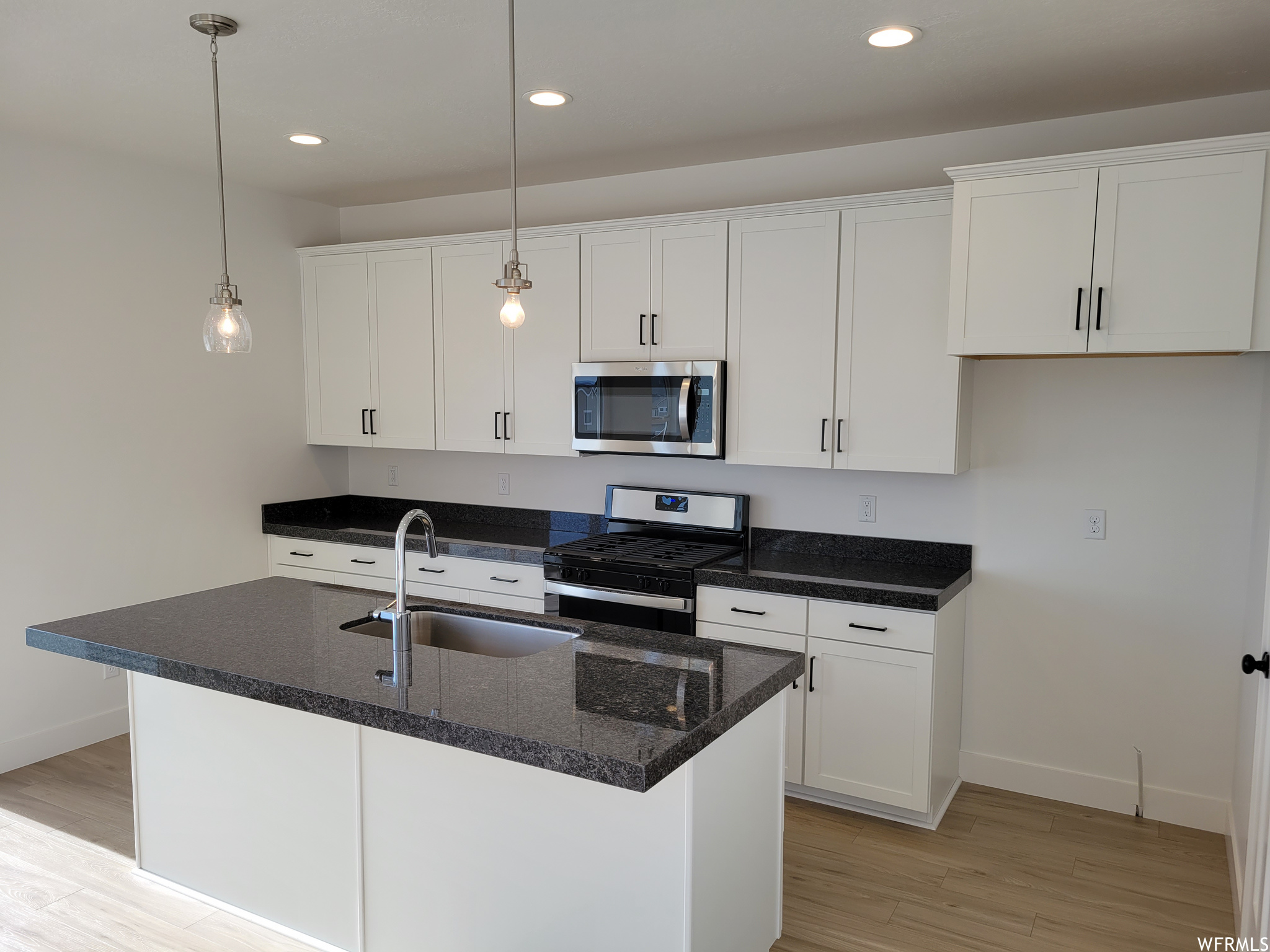 Kitchen featuring microwave, gas range oven, white cabinets, pendant lighting, dark stone countertops, and light parquet floors