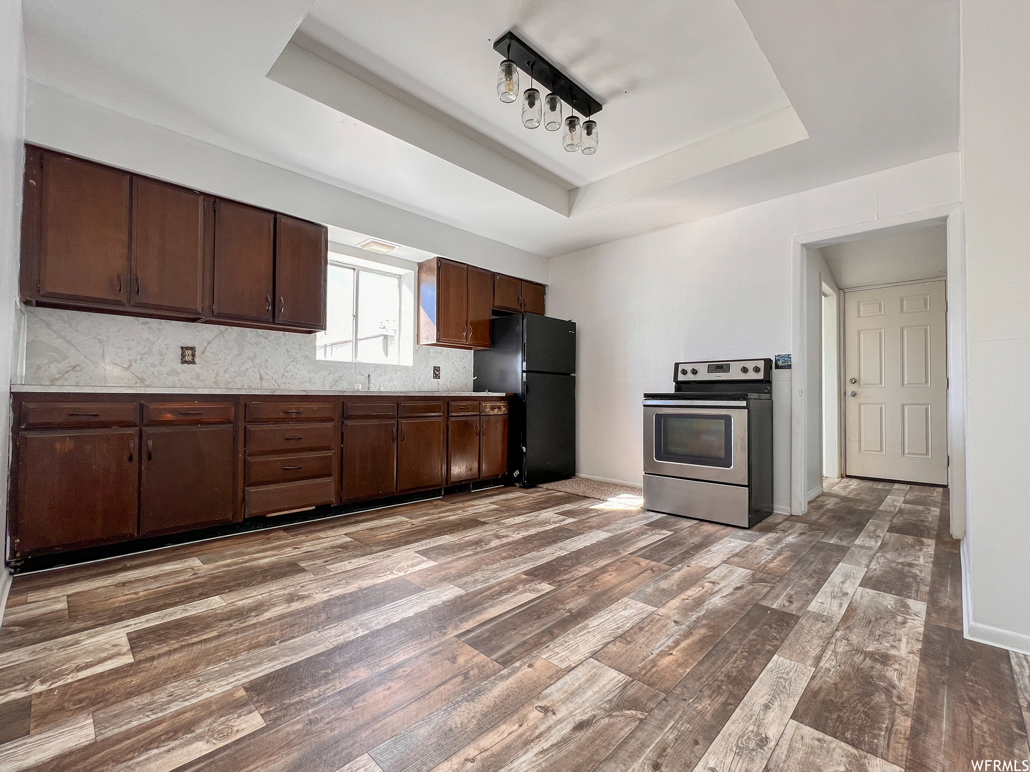 Kitchen featuring natural light, range oven, stainless steel refrigerator, dark flooring, and dark brown cabinetry