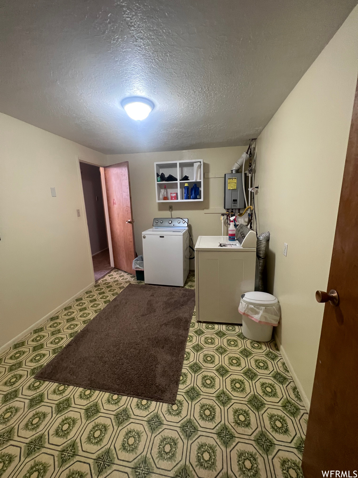 Laundry area featuring dark tile floors, a textured ceiling, independent washer and dryer, water heater, and washer / clothes dryer