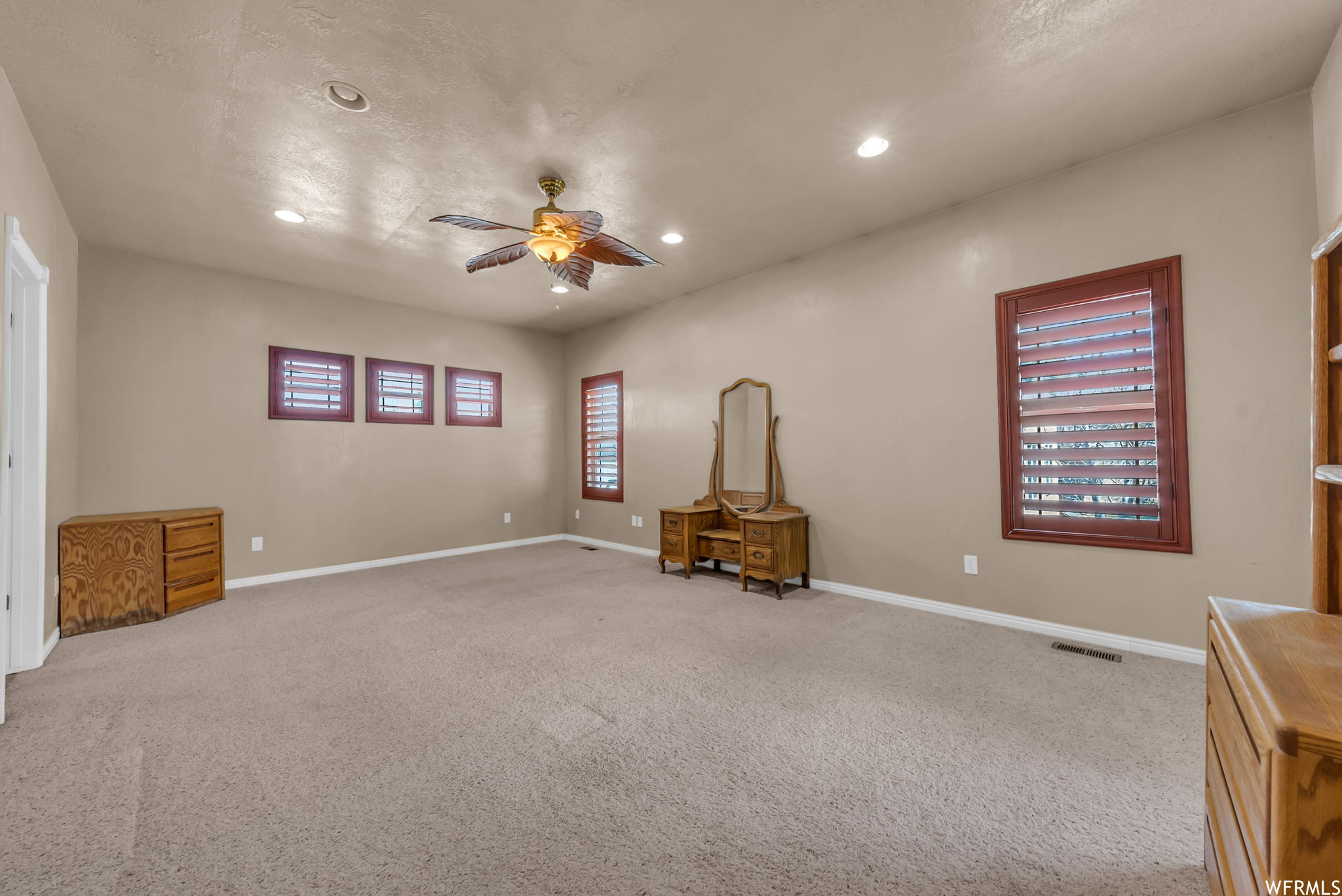 Empty room featuring natural light, carpet, and a ceiling fan