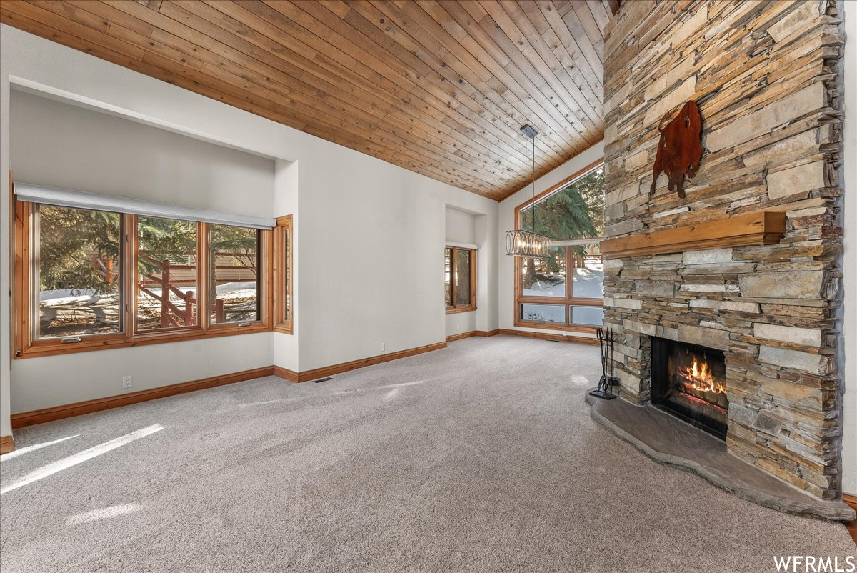 Unfurnished living room featuring wooden ceiling, a stone fireplace, light colored carpet, and plenty of natural light