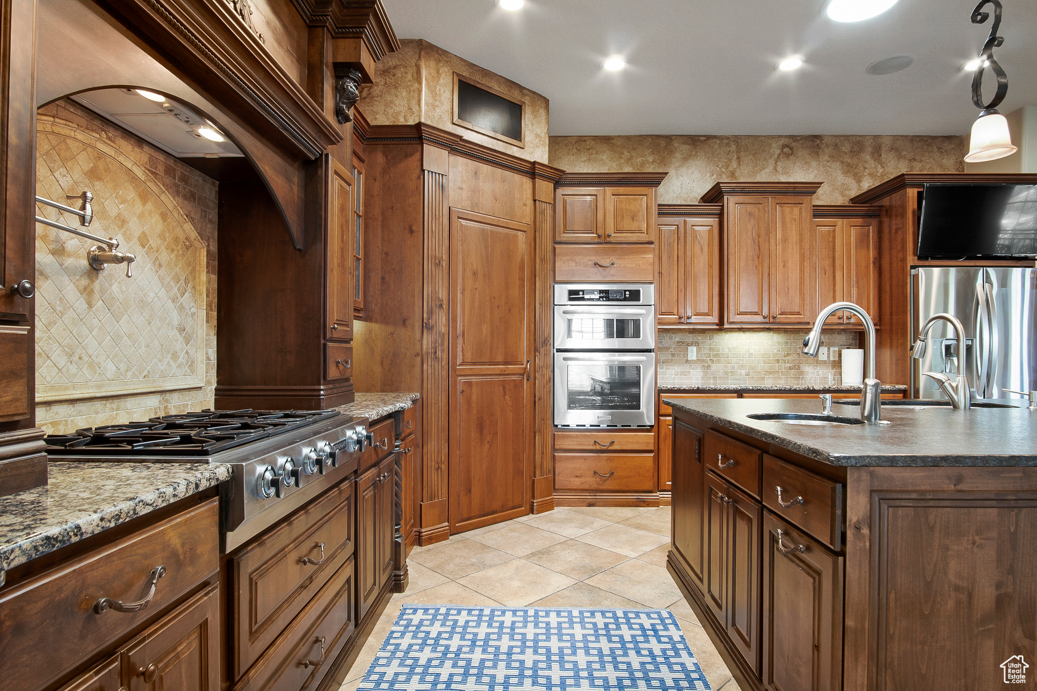 Kitchen featuring dark stone counters, tasteful backsplash, stainless steel appliances, light tile flooring, and a kitchen island with sink