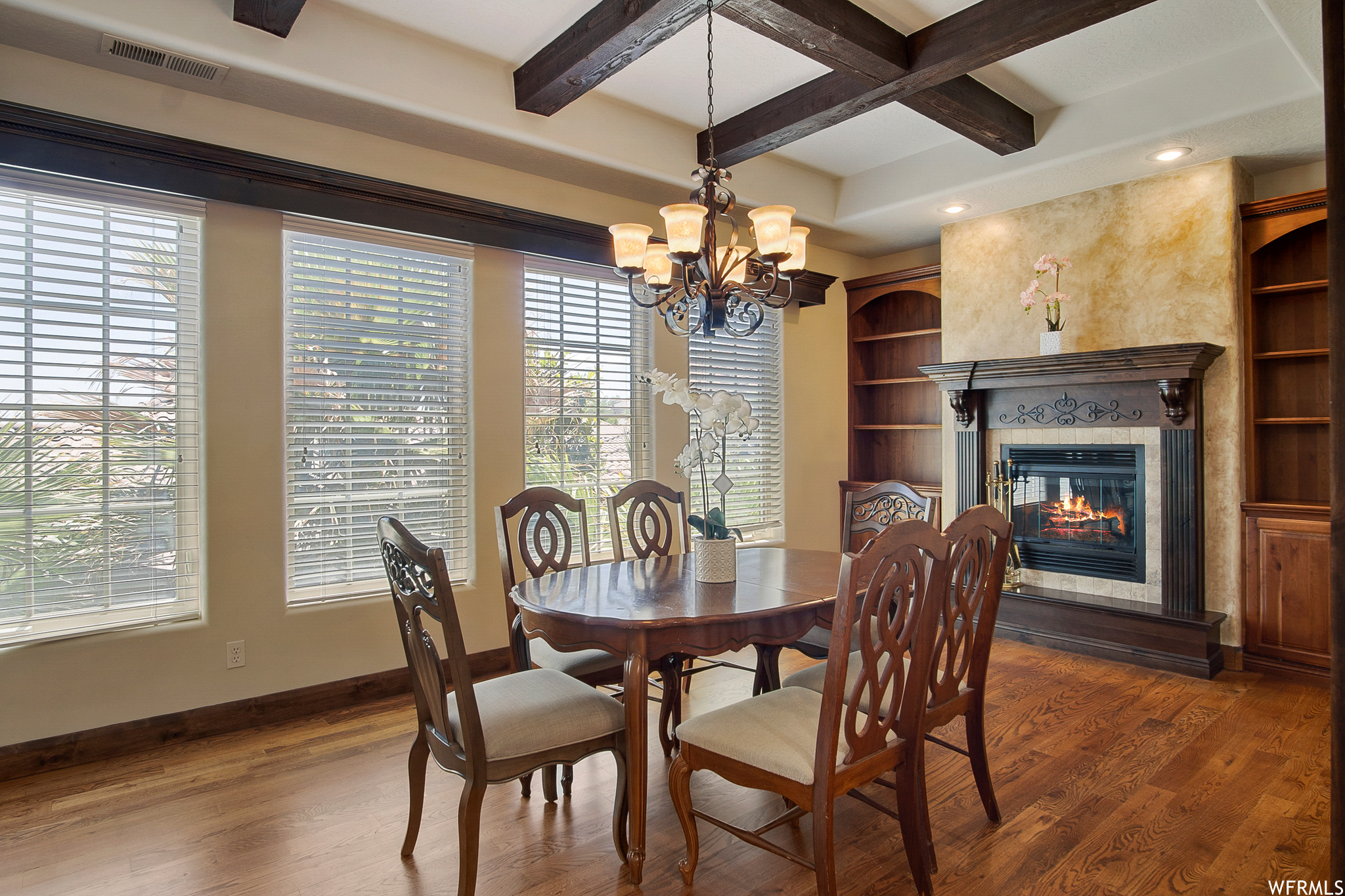 Dining area featuring hardwood flooring, coffered ceiling, a notable chandelier, a fireplace, wood beam ceiling, and natural light