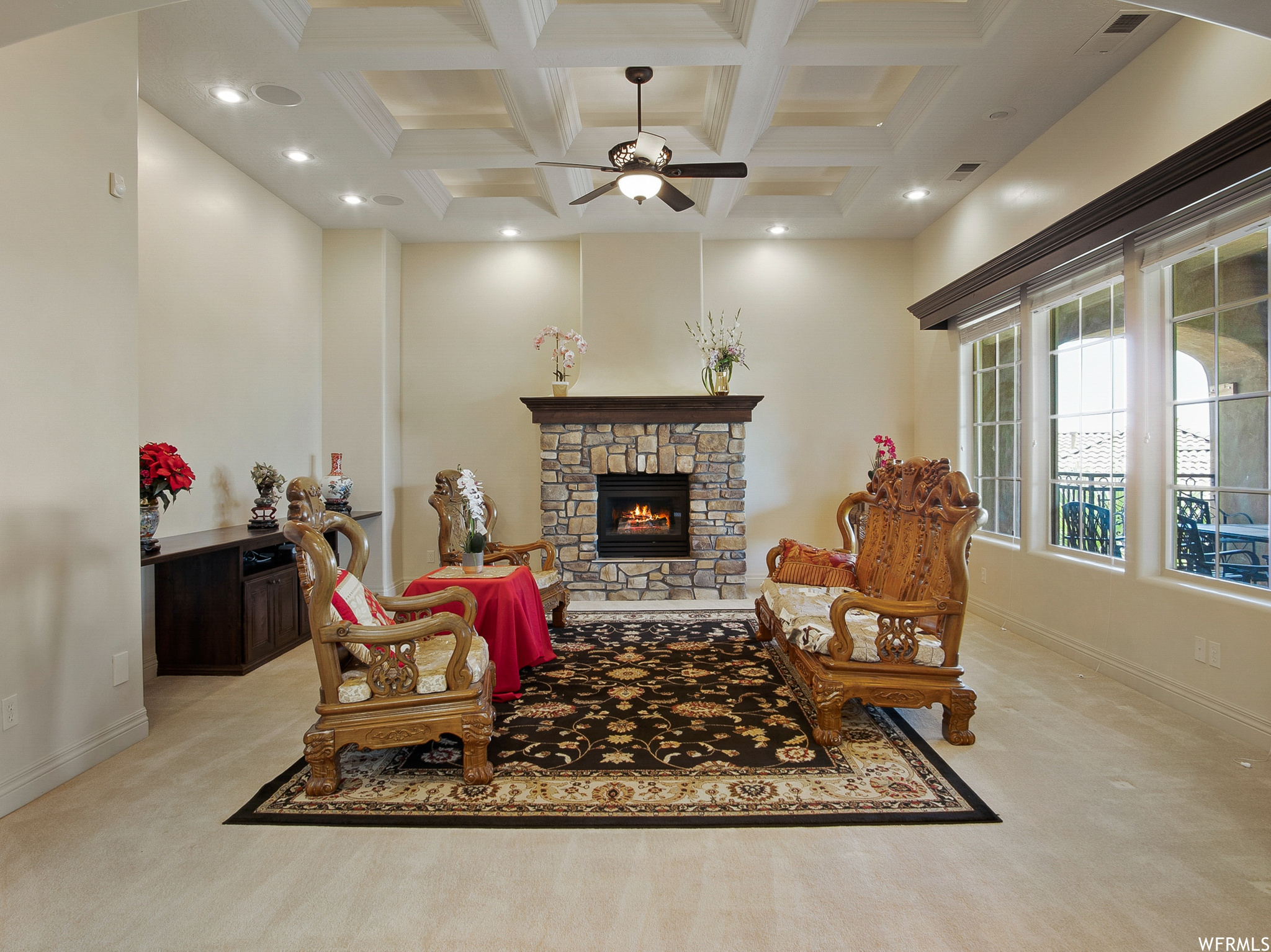 Carpeted living room featuring a fireplace, coffered ceiling, wood beam ceiling, natural light, and a ceiling fan