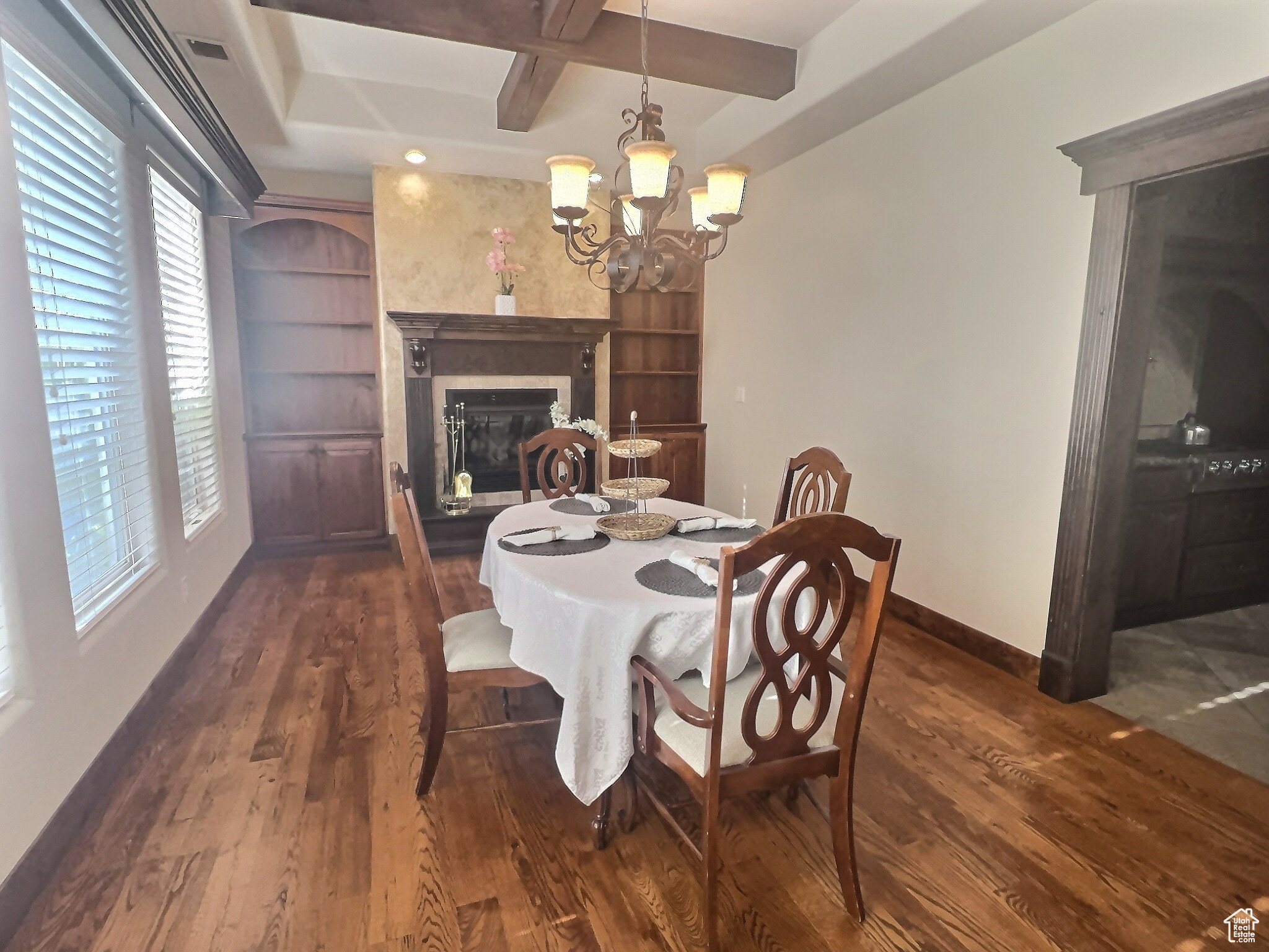 Formal Dining room with a premium fireplace, dark wood-type flooring, a notable chandelier, and a raised ceiling