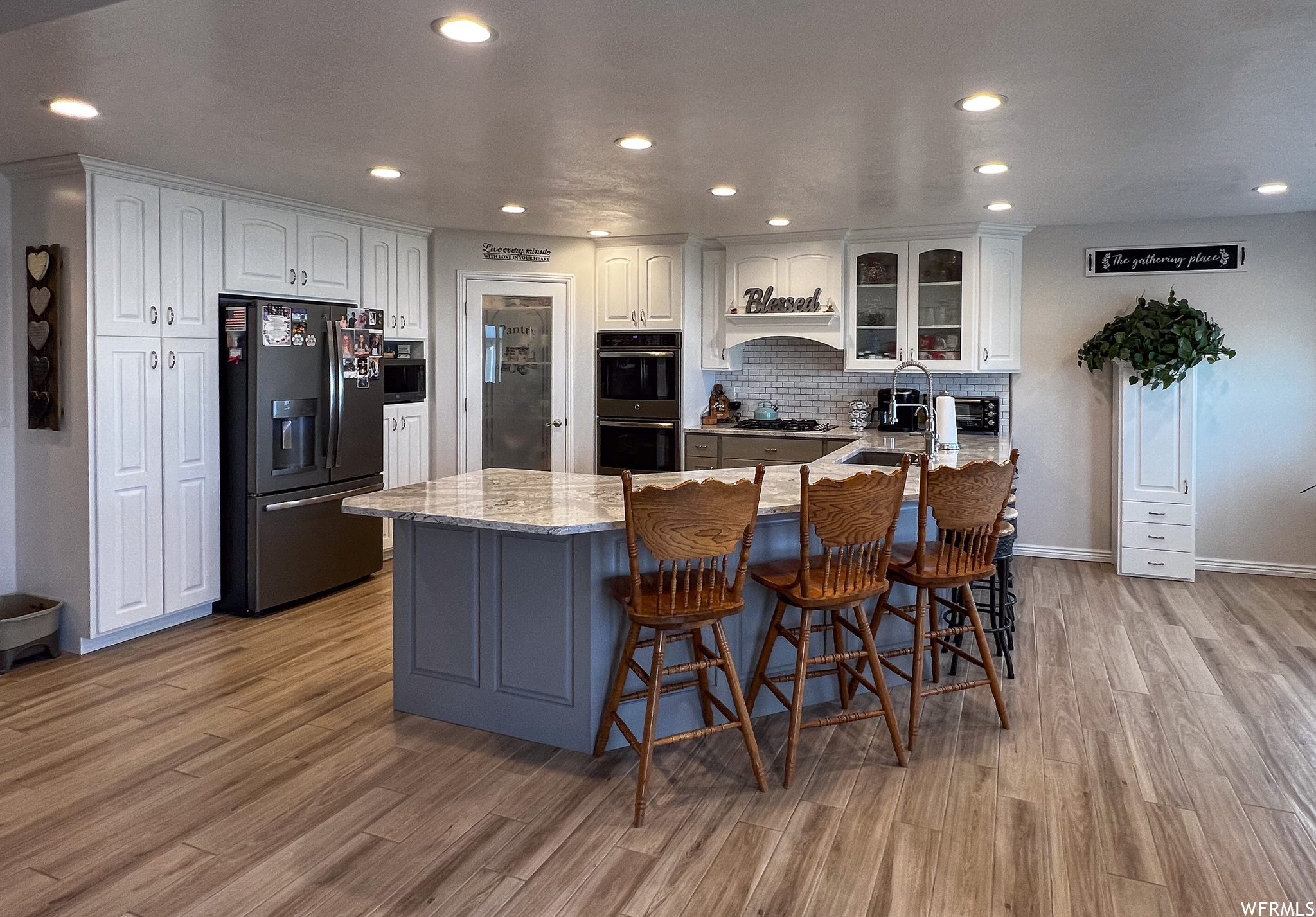 Kitchen with a breakfast bar, refrigerator, double oven, light colored flooring, light stone countertops, and white cabinets