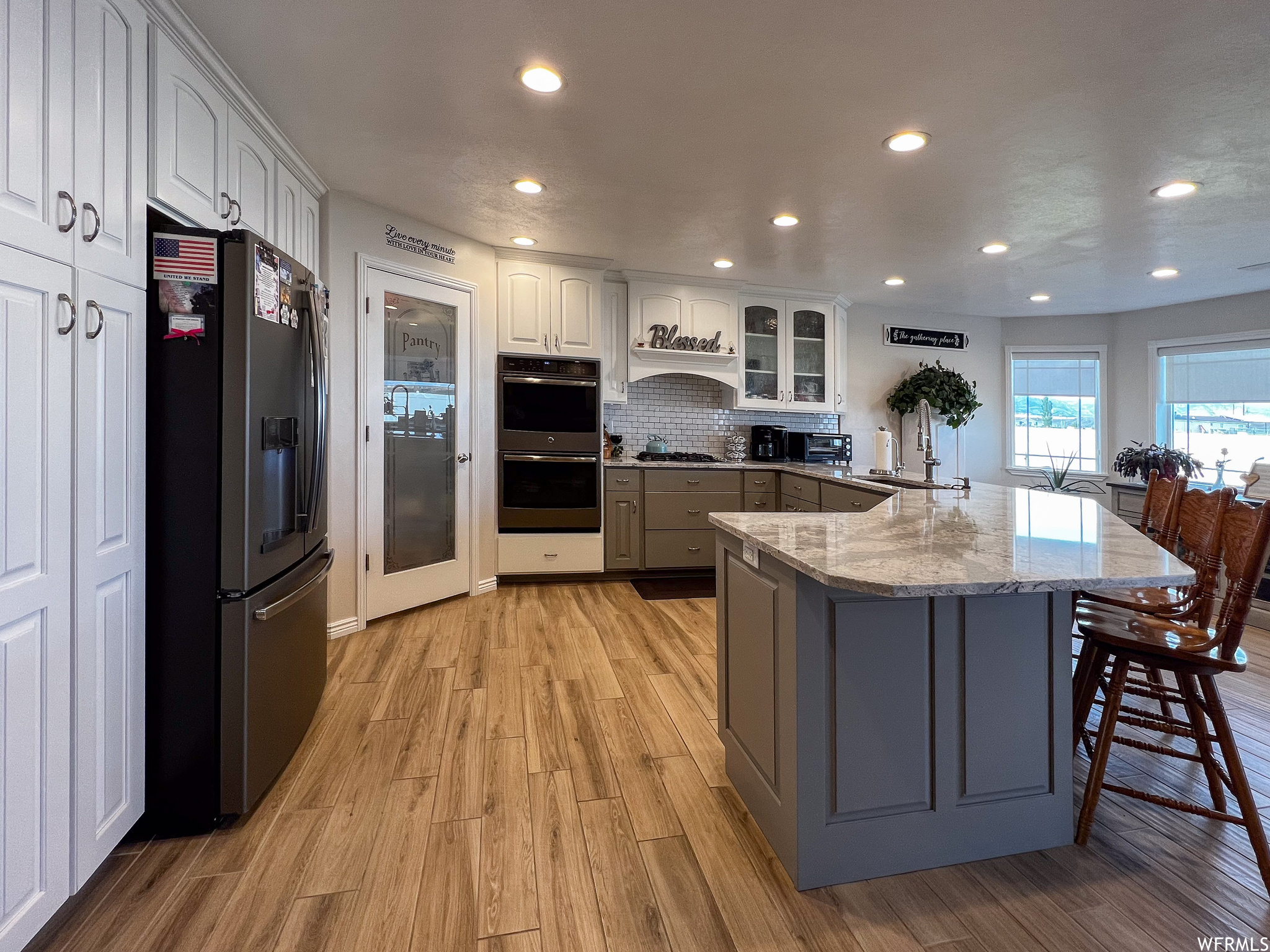 Kitchen featuring a breakfast bar, refrigerator, double oven, light colored floors, white cabinets, and stone countertops