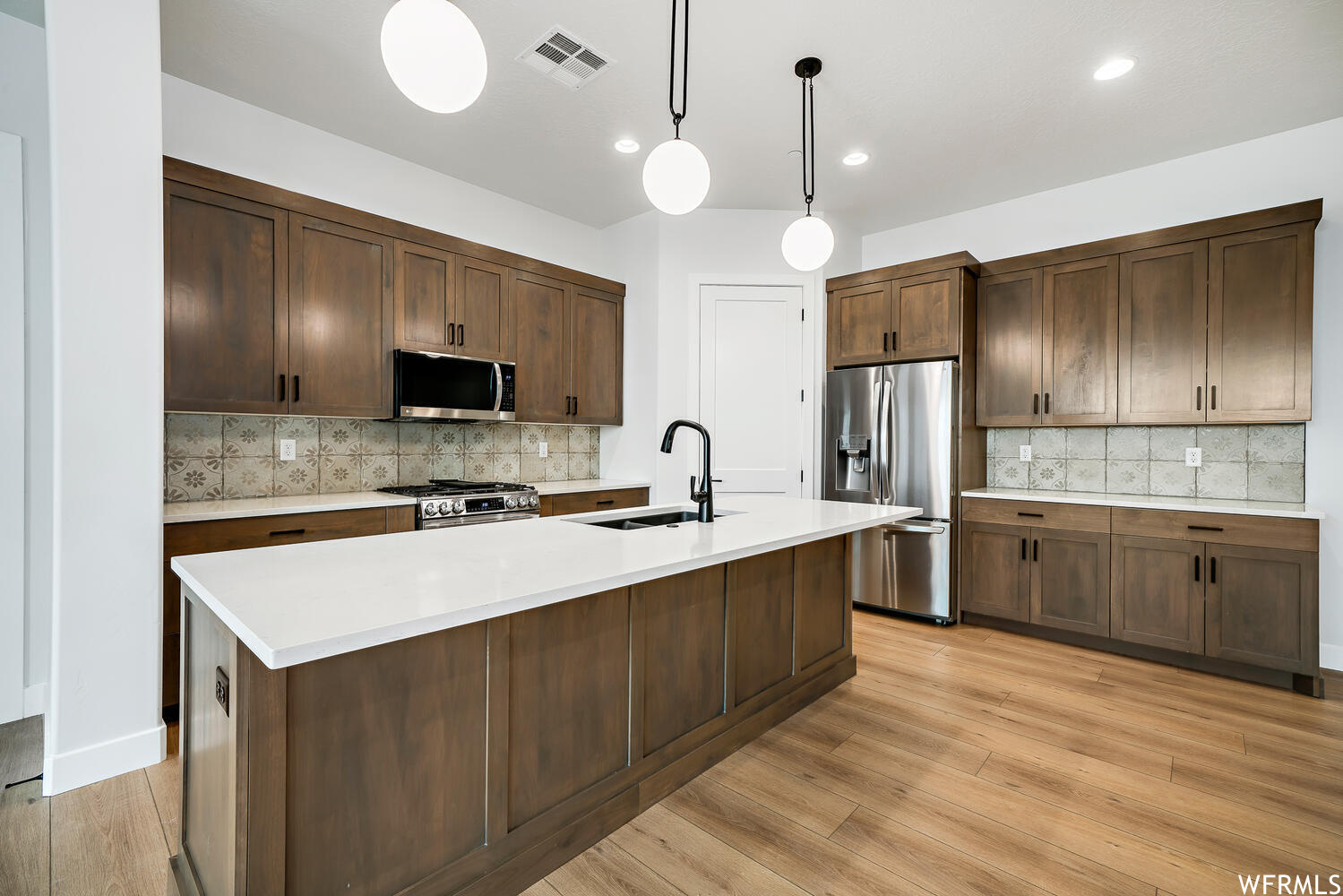 Kitchen featuring refrigerator, range oven, microwave, pendant lighting, light hardwood floors, and light countertops