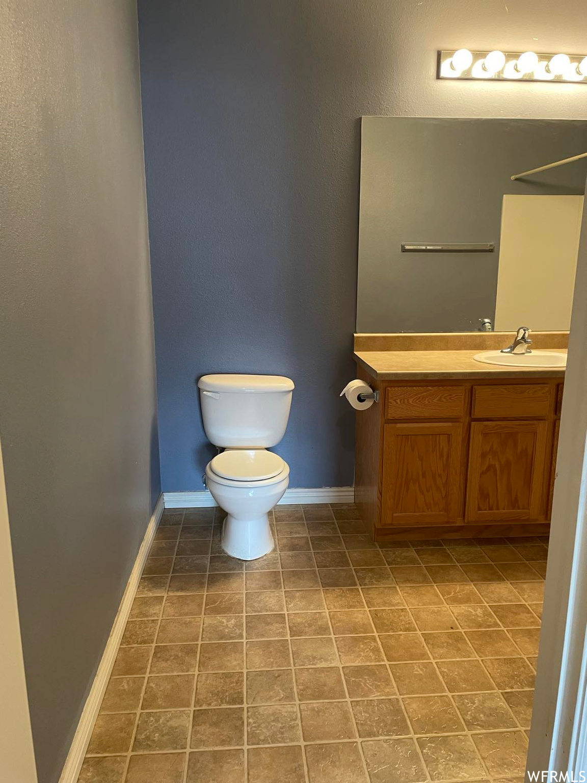 Half bathroom featuring tile floors, toilet, vanity with extensive cabinet space, and mirror