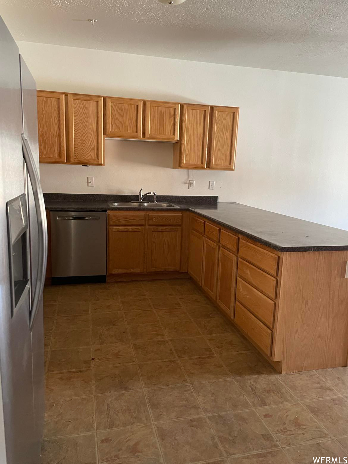Kitchen featuring tile flooring, stainless steel dishwasher, refrigerator, and brown cabinets