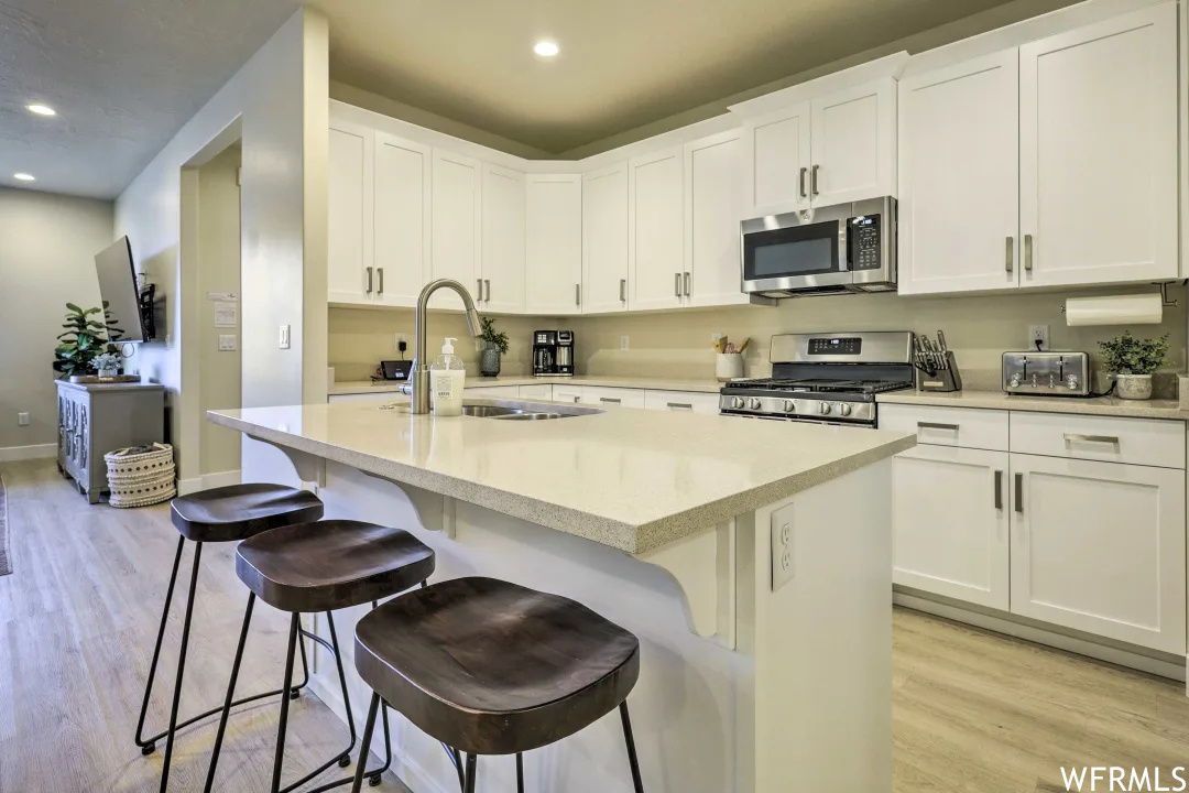 Kitchen featuring a kitchen bar, TV, stainless steel microwave, gas range oven, white cabinets, light countertops, and light hardwood floors