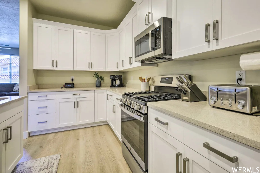 Kitchen with microwave, gas range oven, white cabinetry, light parquet floors, and light countertops