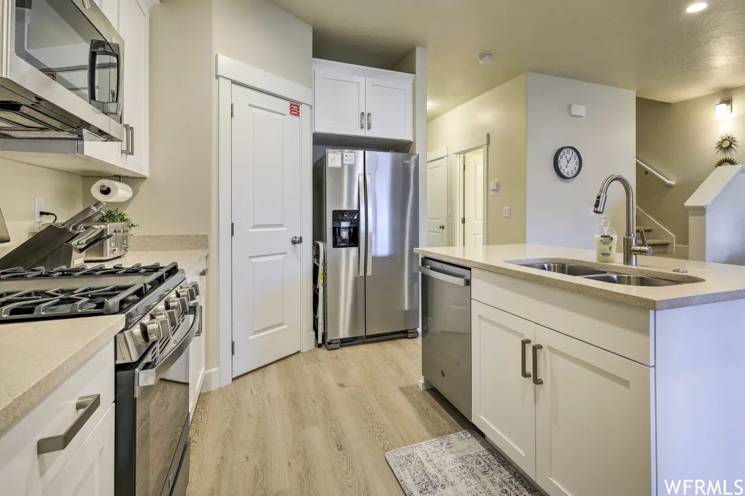 Kitchen featuring microwave, dishwasher, refrigerator, gas range oven, light countertops, light parquet floors, and white cabinetry