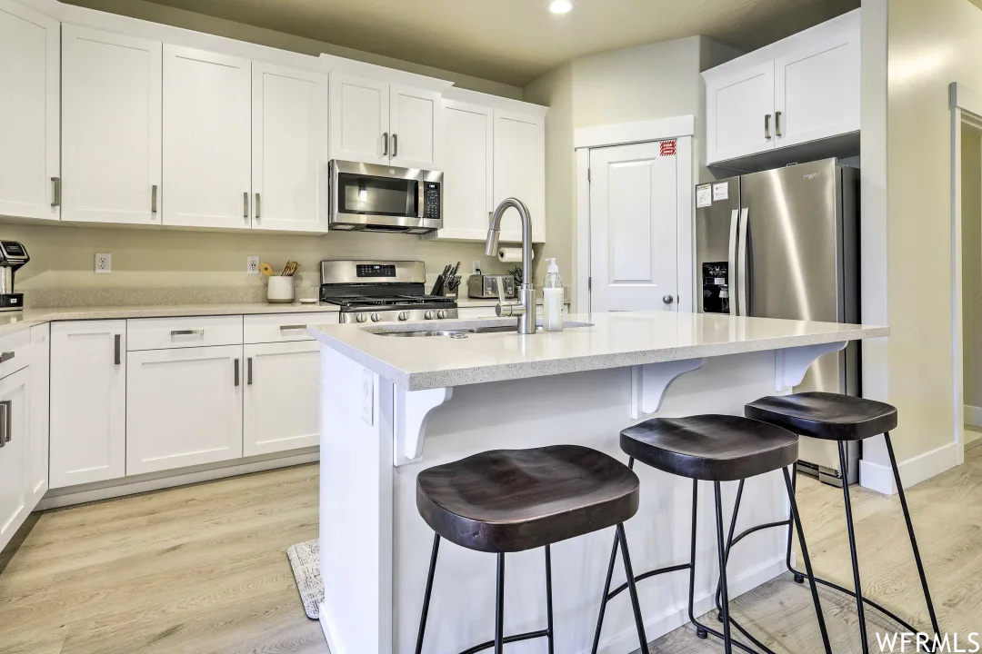 Kitchen featuring a breakfast bar area, microwave, range oven, white cabinets, light floors, and light quartz countertops