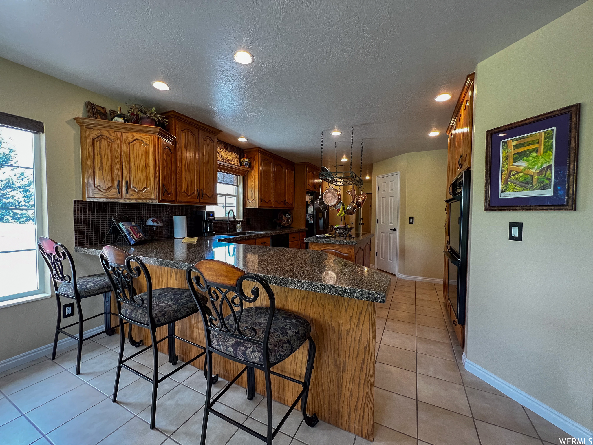 Kitchen featuring natural light, a breakfast bar area, light tile floors, brown cabinets, and dark countertops