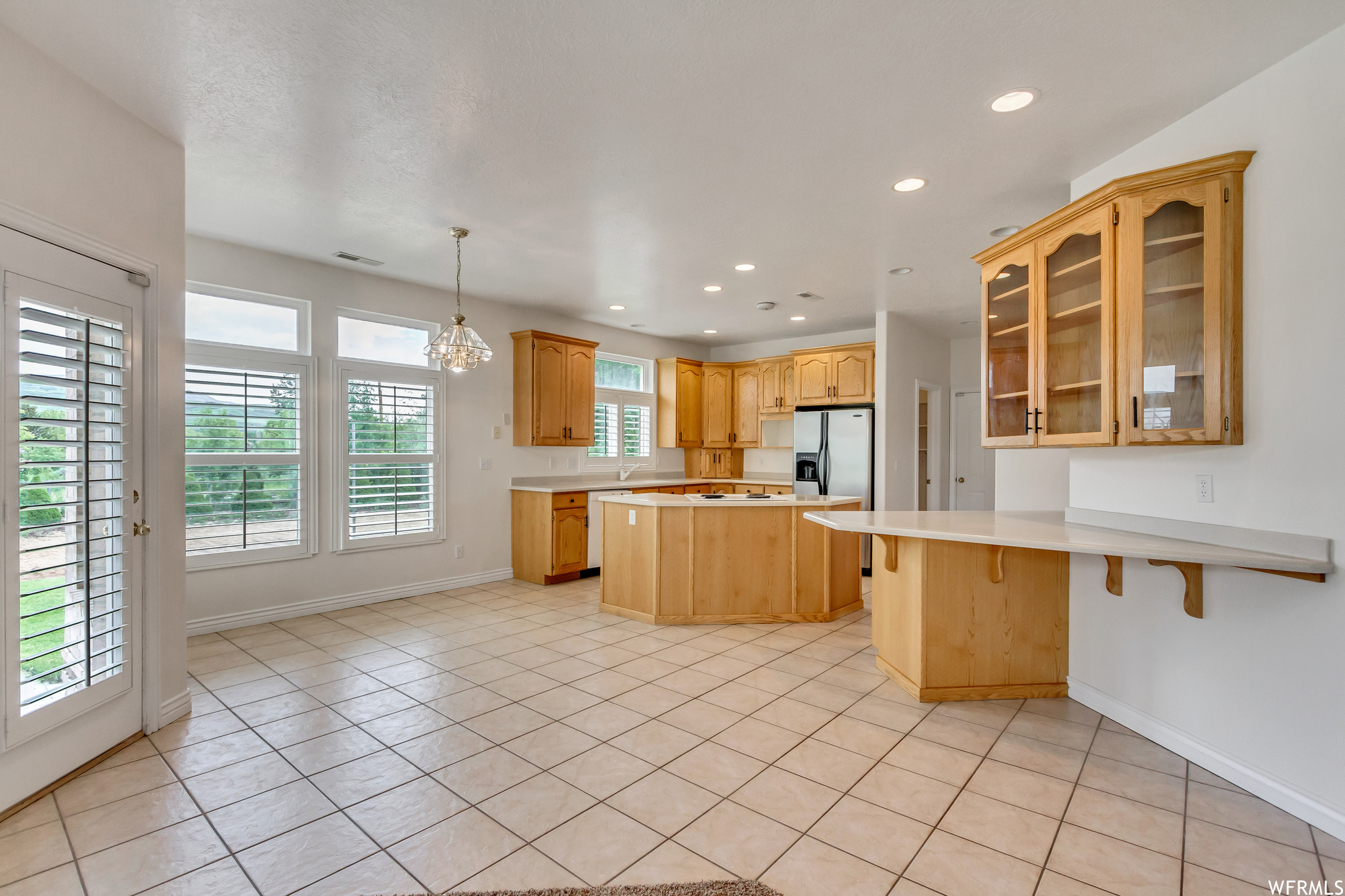 Kitchen with plenty of natural light, light countertops, light tile floors, brown cabinetry, and pendant lighting