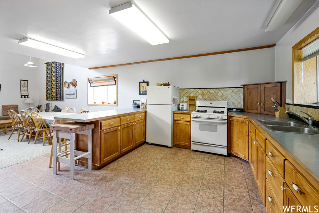 Kitchen with a kitchen breakfast bar, natural light, refrigerator, gas range oven, brown cabinets, and light tile floors