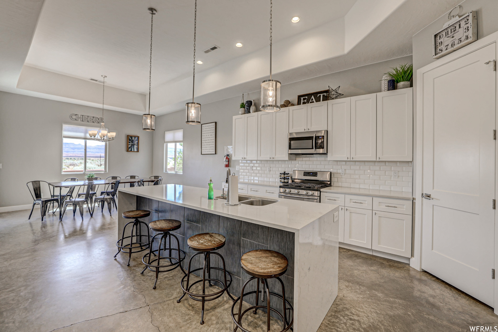 Kitchen featuring a kitchen bar, plenty of natural light, microwave, gas range oven, light countertops, white cabinetry, light tile flooring, and pendant lighting