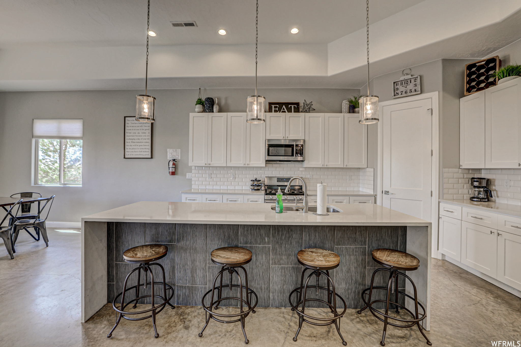 Kitchen featuring natural light, a center island, a kitchen breakfast bar, stainless steel microwave, range oven, light countertops, light tile floors, pendant lighting, and white cabinets