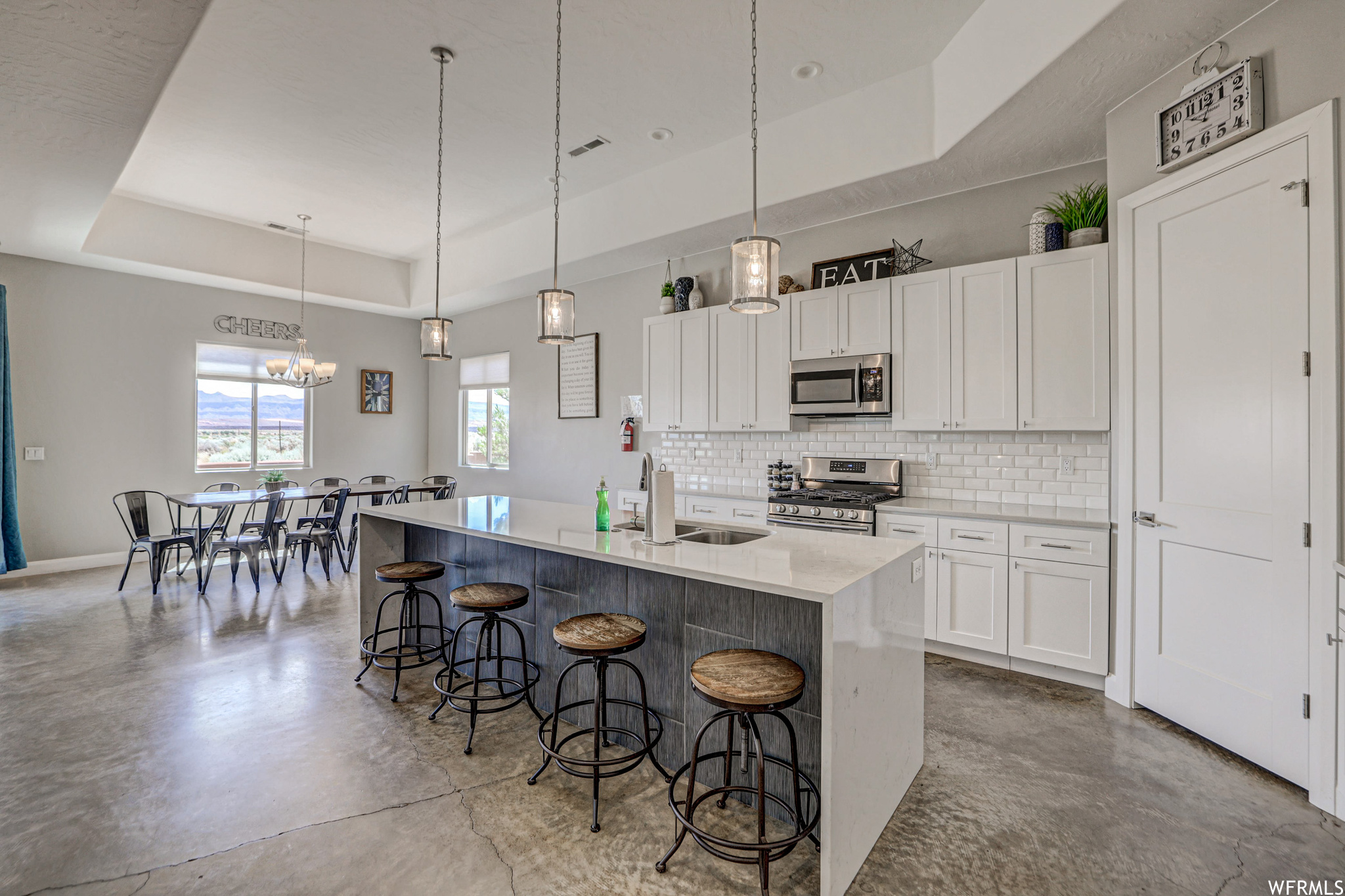 Kitchen with a breakfast bar, natural light, a center island, gas range oven, microwave, light countertops, light tile floors, pendant lighting, and white cabinetry
