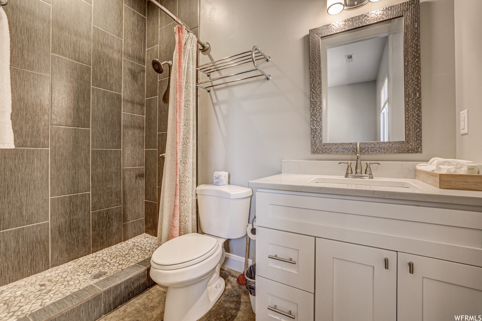 Bathroom with toilet, vanity with extensive cabinet space, shower curtain, mirror, and a shower