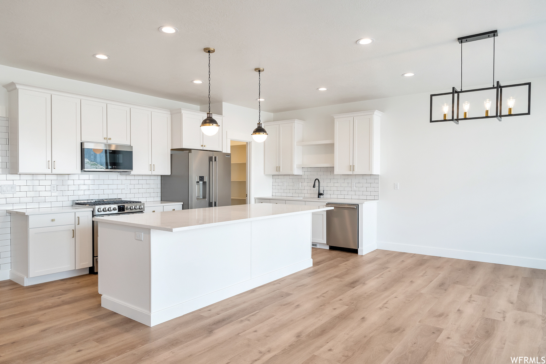 Kitchen featuring a kitchen island, refrigerator, stainless steel dishwasher, gas range oven, microwave, light countertops, light parquet floors, pendant lighting, and white cabinets