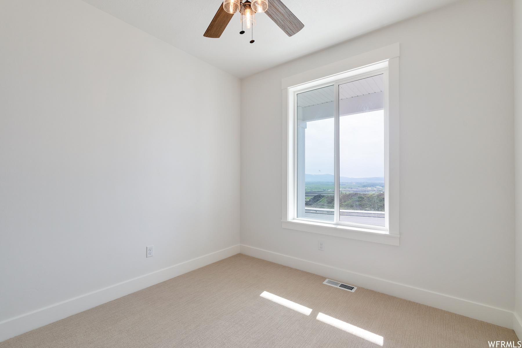 Empty room with natural light, carpet, and a ceiling fan