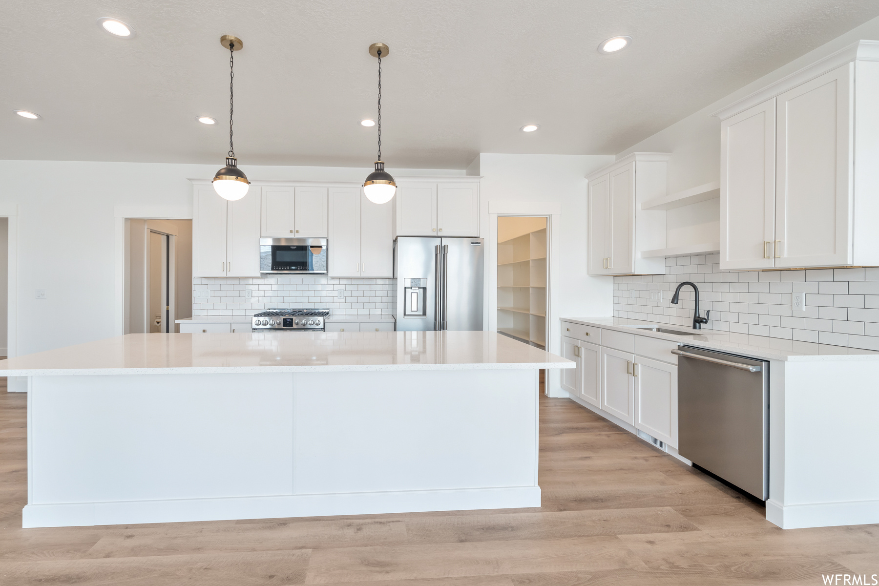Kitchen featuring refrigerator, stainless steel dishwasher, microwave, light countertops, light hardwood flooring, pendant lighting, and white cabinets