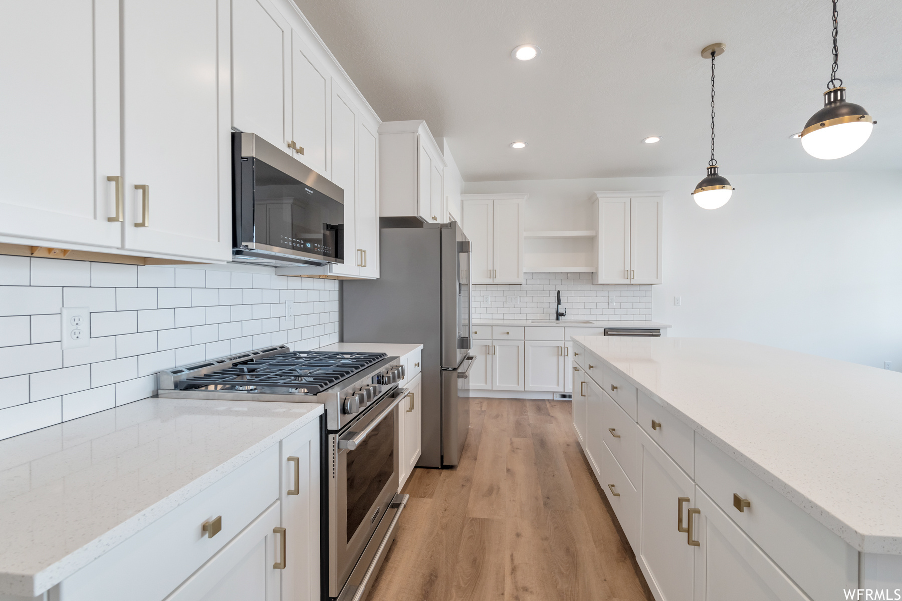 Kitchen with microwave, gas range oven, light countertops, white cabinets, light parquet floors, and pendant lighting