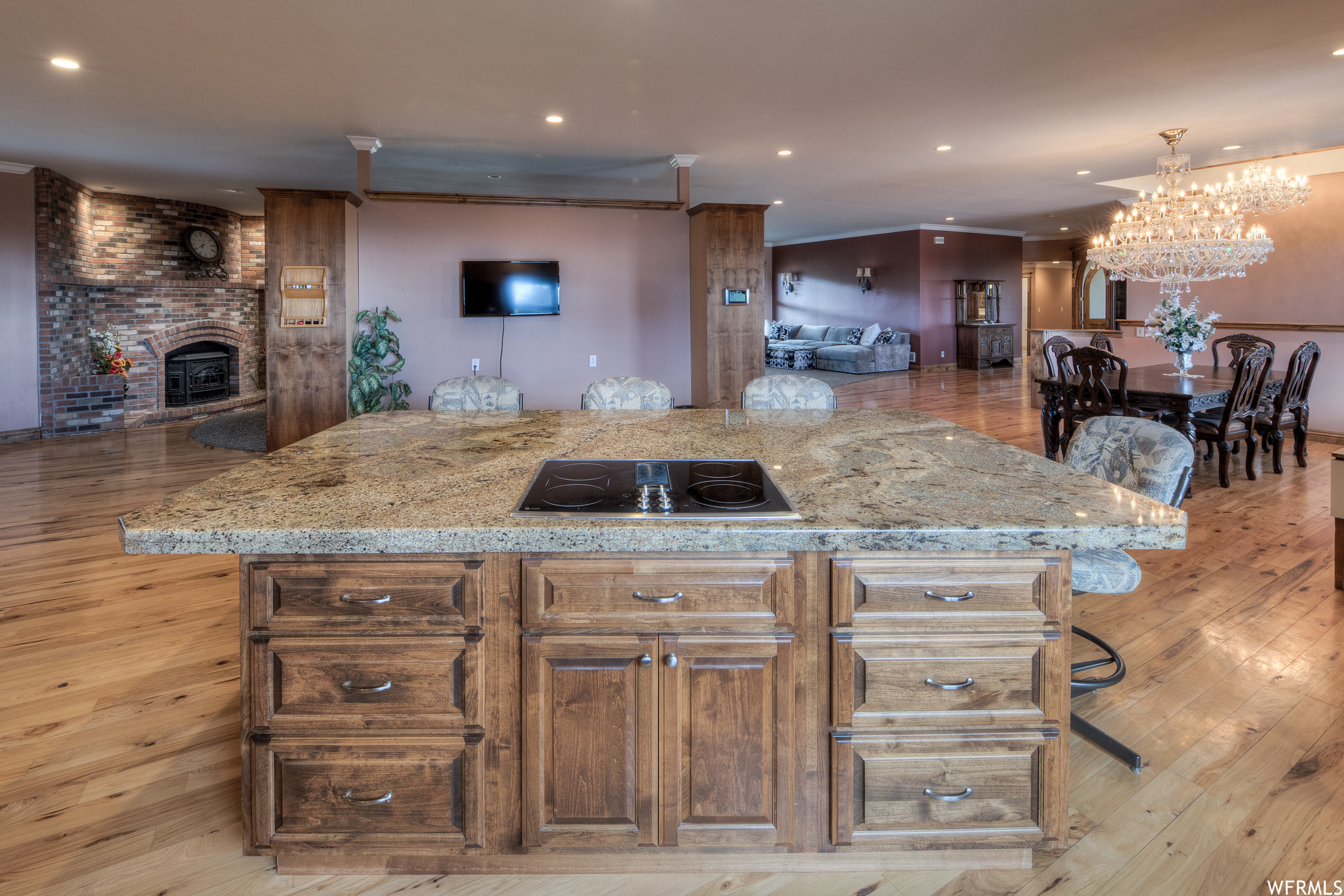 Kitchen with a kitchen bar, a chandelier, a brick fireplace, electric cooktop, TV, light hardwood floors, and light stone countertops