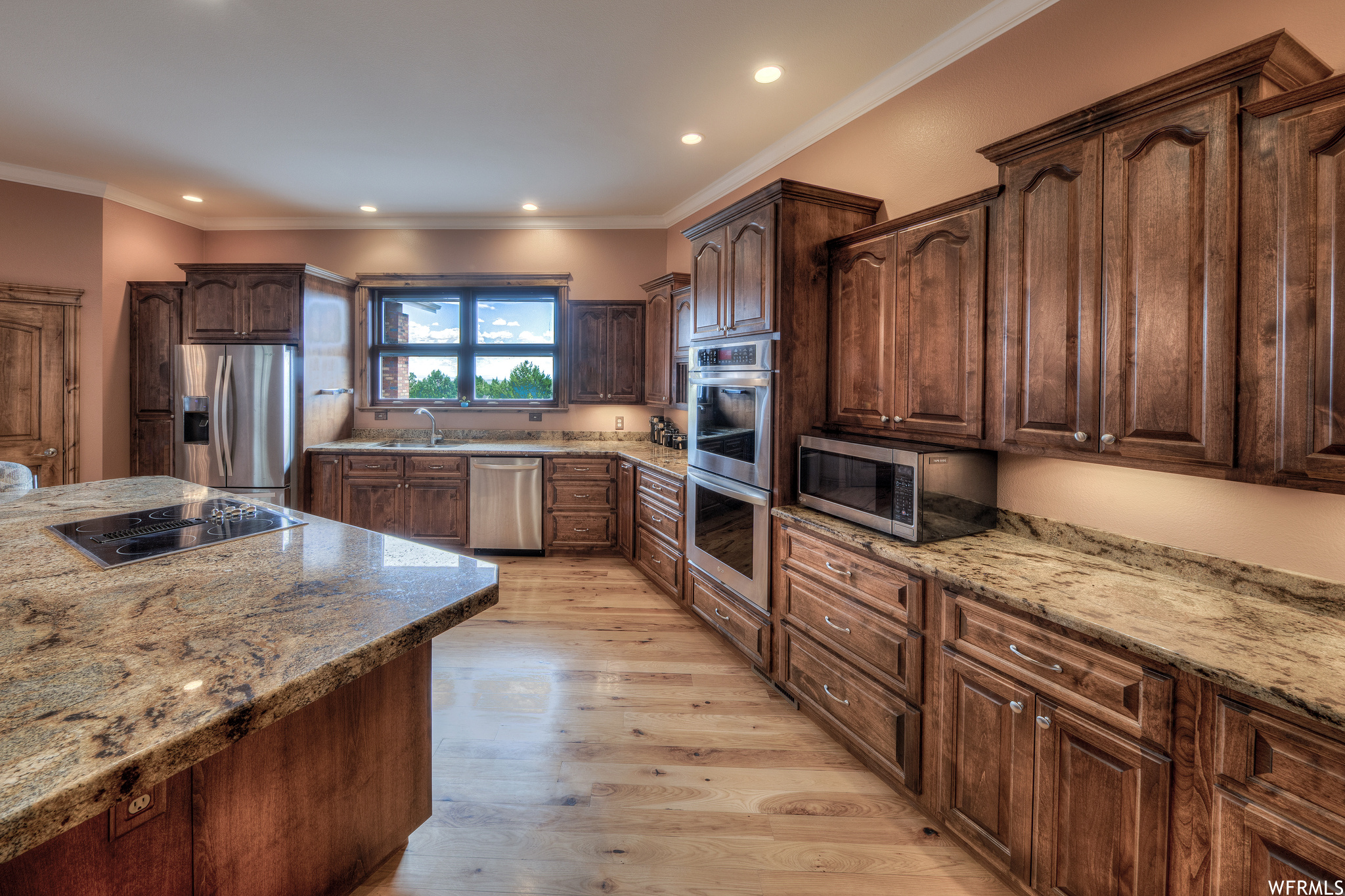 Kitchen with natural light, double oven, microwave, stainless steel refrigerator, dishwasher, electric stovetop, stone countertops, light parquet floors, and dark brown cabinetry