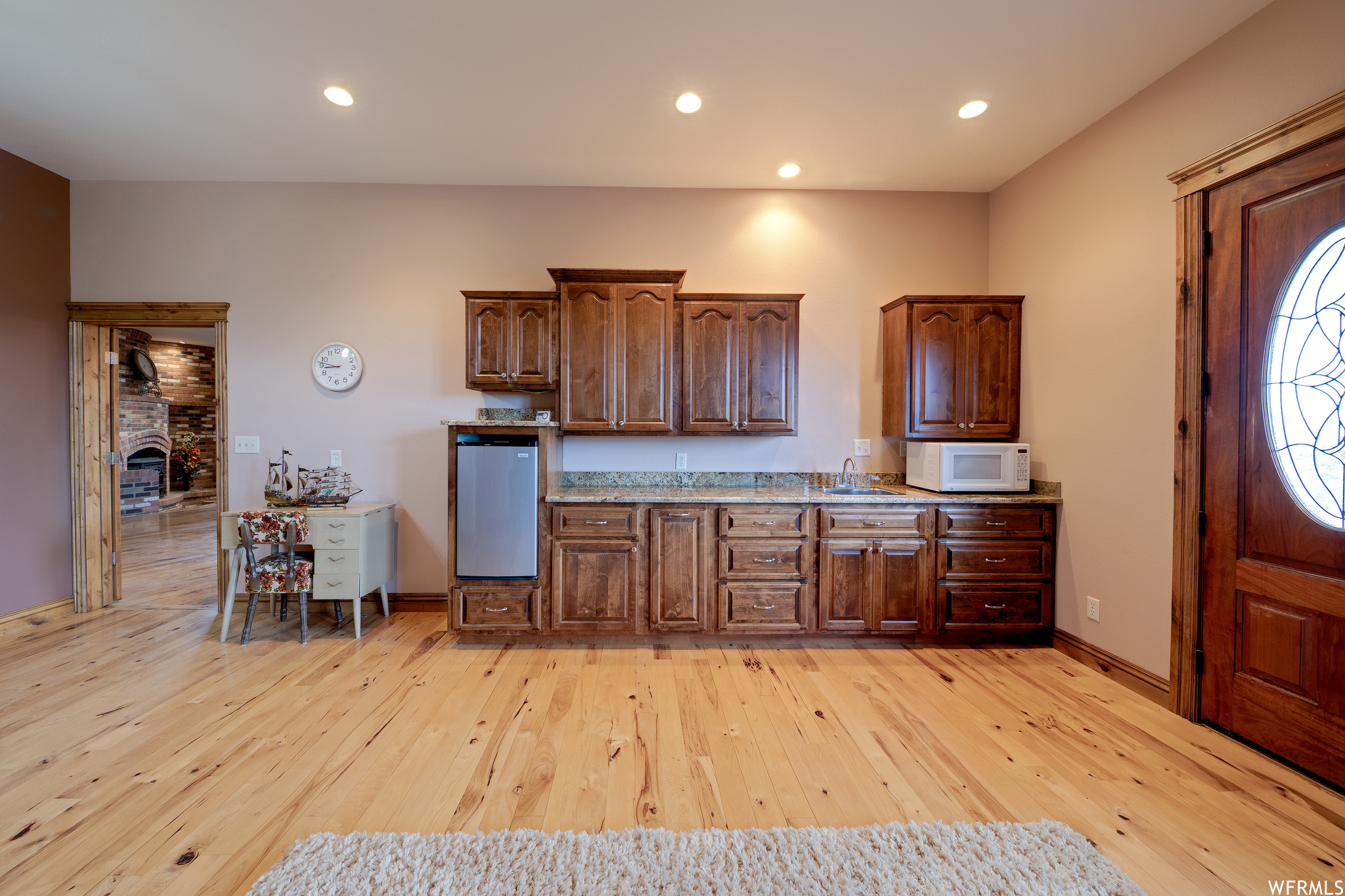 Kitchen featuring a fireplace, natural light, microwave, dark brown cabinetry, and light hardwood flooring