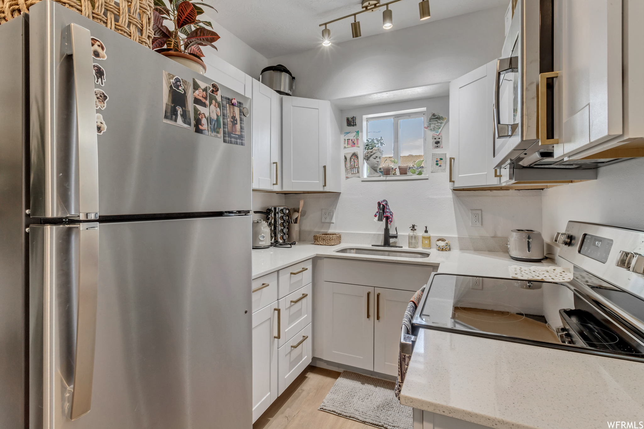Kitchen featuring electric range oven, refrigerator, light hardwood flooring, white cabinetry, and light countertops