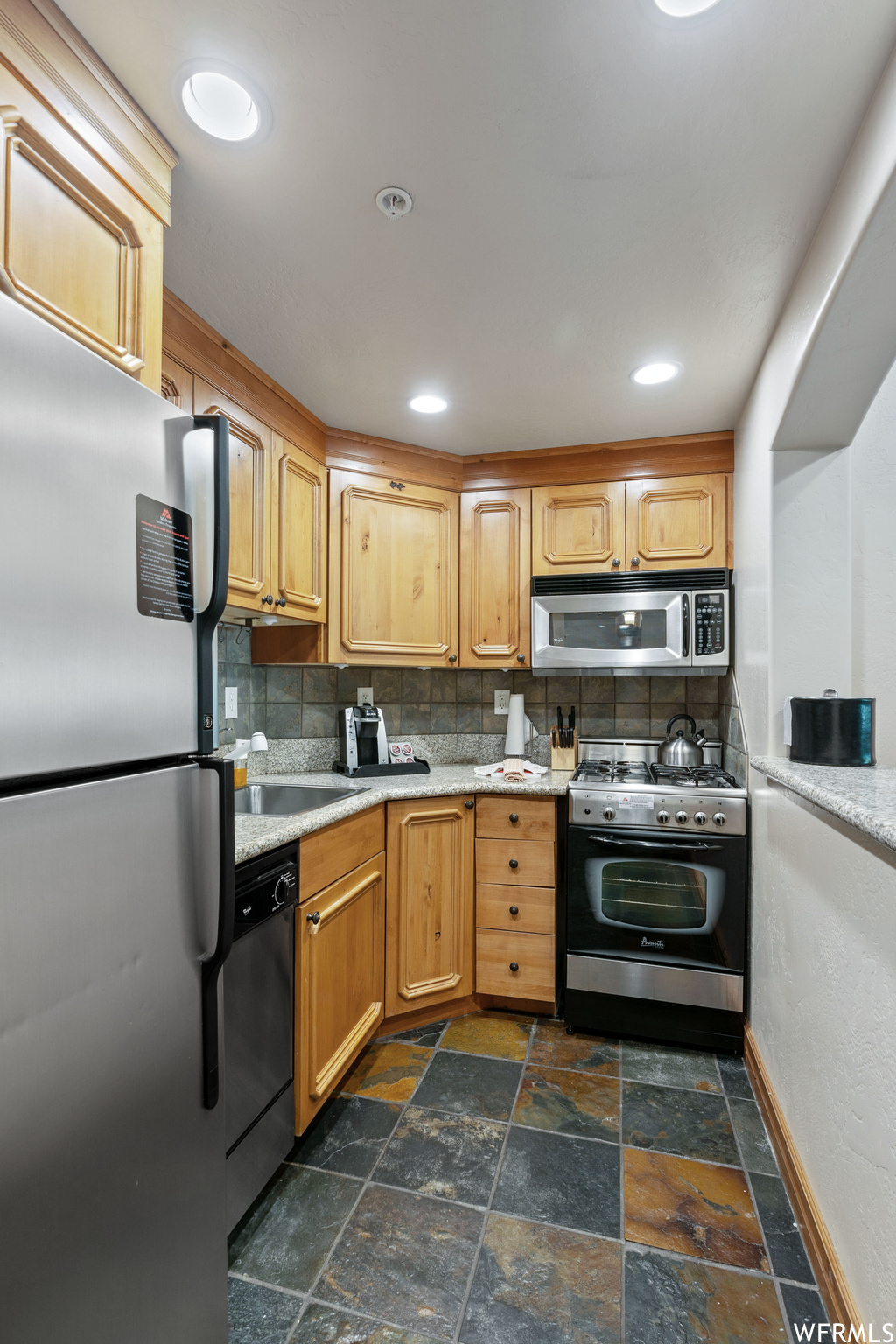 Kitchen with microwave, dishwasher, refrigerator, gas range oven, light countertops, and dark tile floors