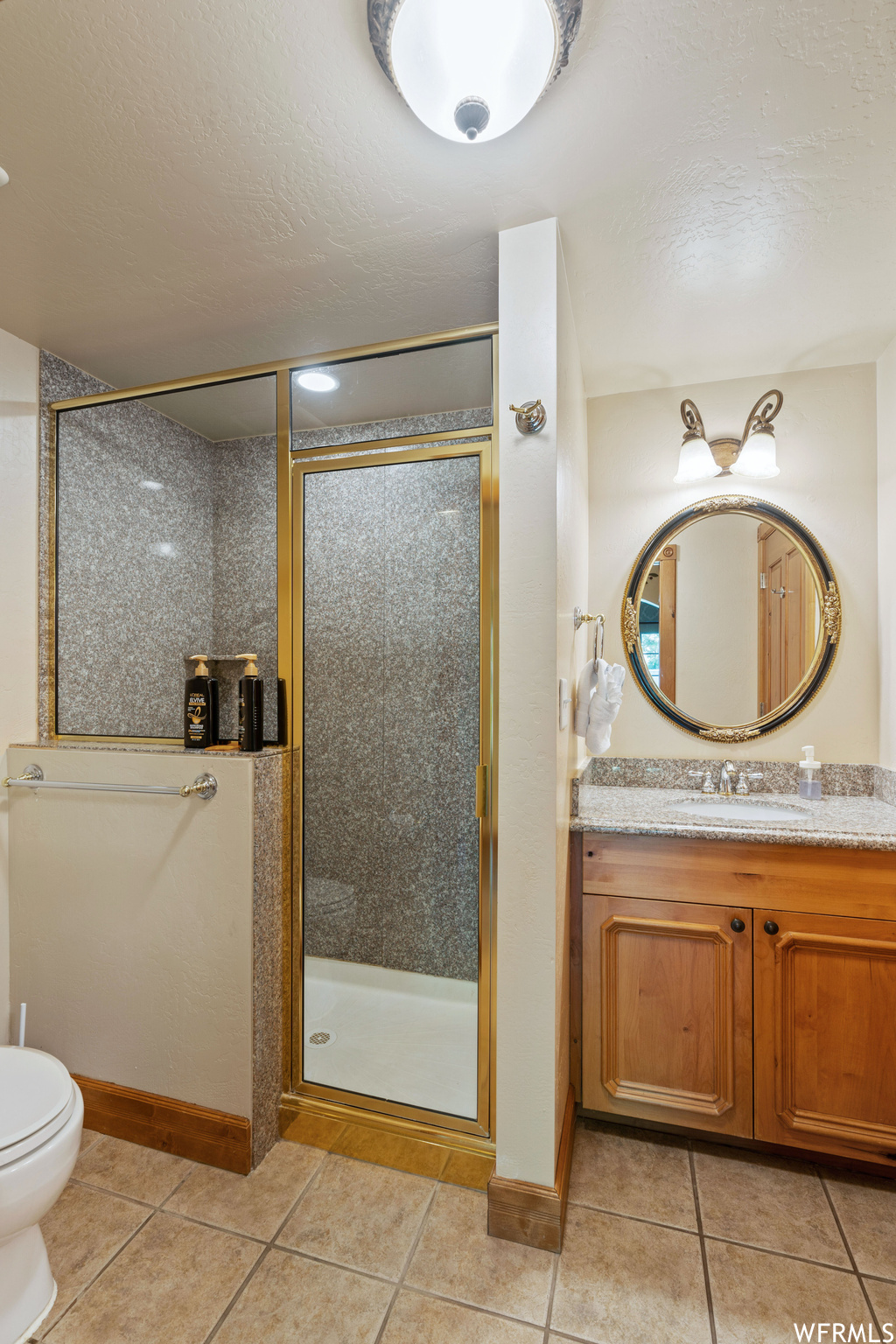 Full bathroom featuring tile floors, mirror, vanity, toilet, and shower with glass door