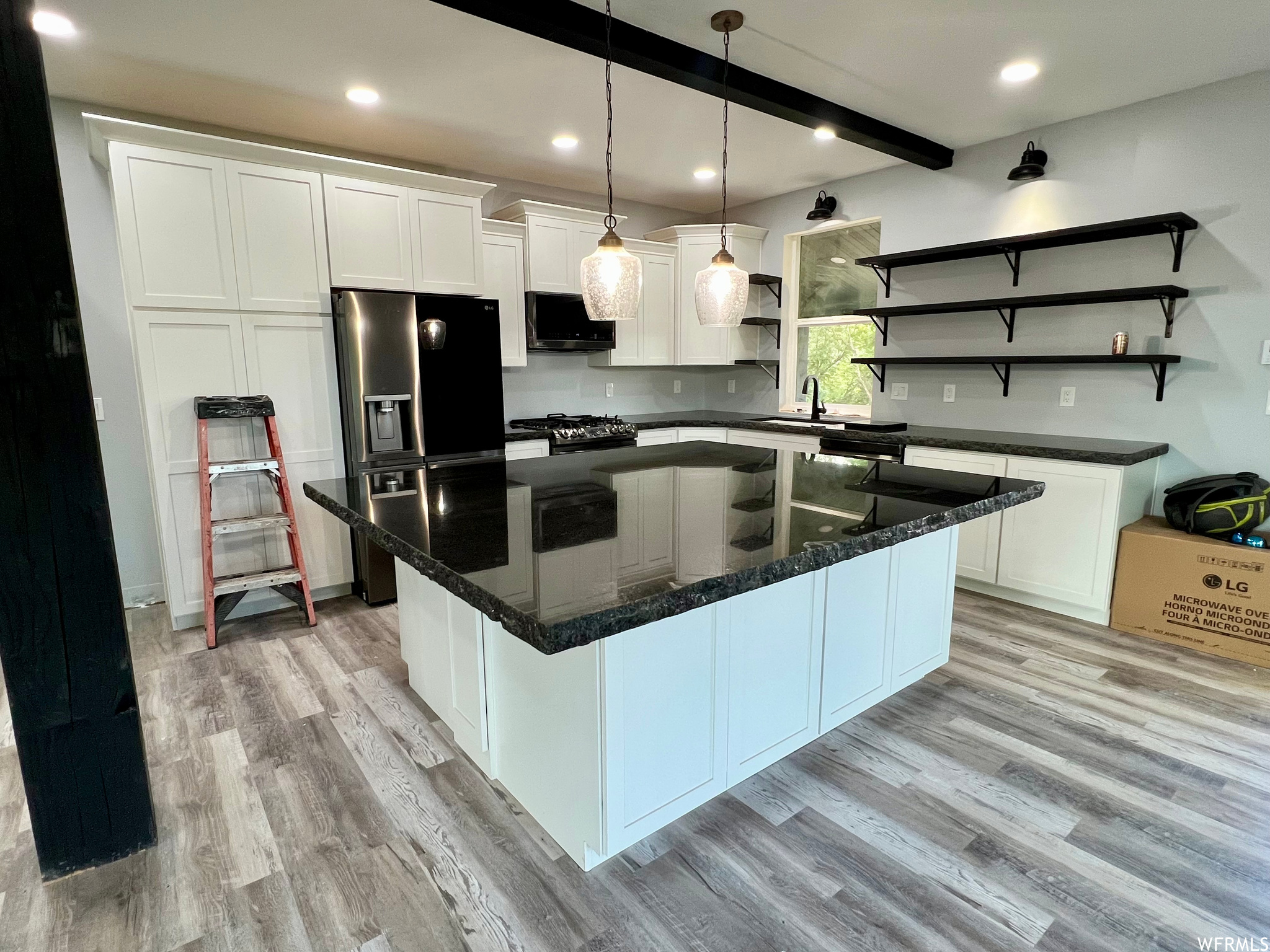 Kitchen with a center island, hardwood floors, dark stone countertops, white cabinets, and pendant lighting
